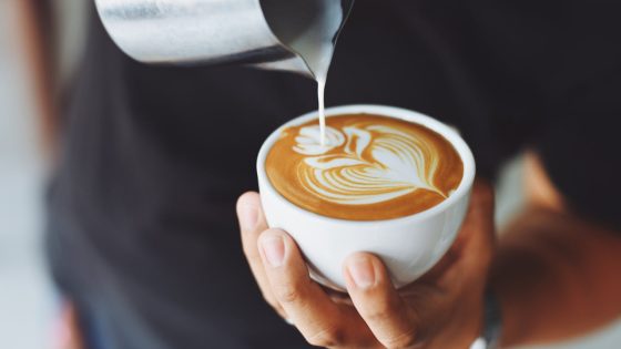 Barista ruošia latte su meno piešiniu – išskirtinis skonis ir jauki atmosfera geriausiose kavinėse Vilniuje.