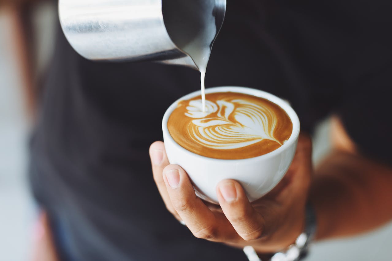 Barista ruošia latte su meno piešiniu – išskirtinis skonis ir jauki atmosfera geriausiose kavinėse Vilniuje.