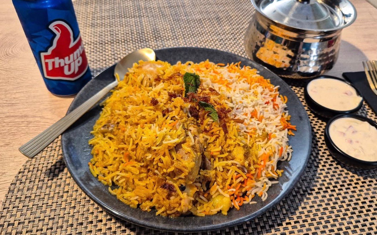 Indiškas biryani ryžių patiekalas su padažais ir Thums Up gėrimu restorane Vilniuje.