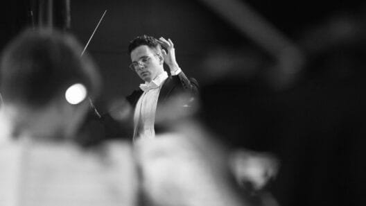 Dirigentas diriguoja orkestrui koncerto metu – Marius Reklaitis įamžintas intensyvios muzikos akimirkos centre.