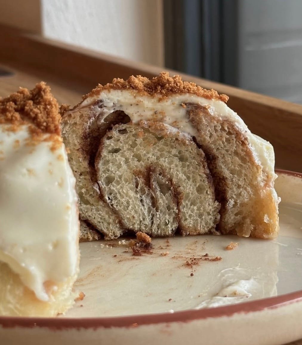 Dvi bandelės kepykla, lėkštėje patiekta didelė, puri ir minkšta cinamoninė bandelė