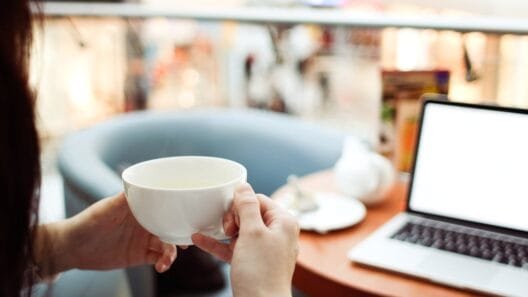 Moderni kavinė darbui Vilniuje su nešiojamu kompiuteriu ir puodeliu kavos ant medinio stalo.