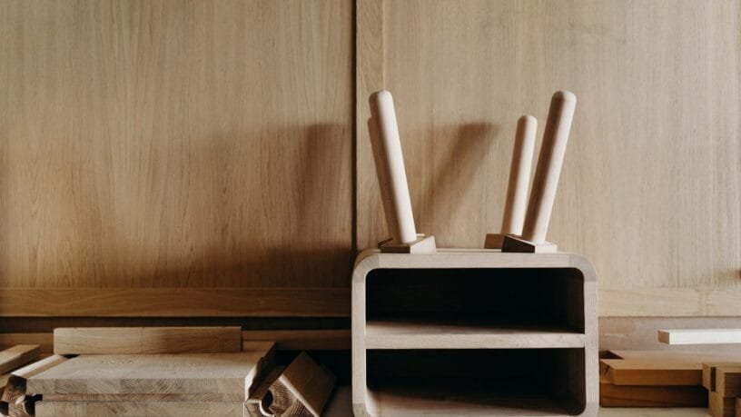 Modernus lietuviškas dizainas namams - natūralaus medžio stalas ir lininės tekstilės detalės šviesiame kambaryje.