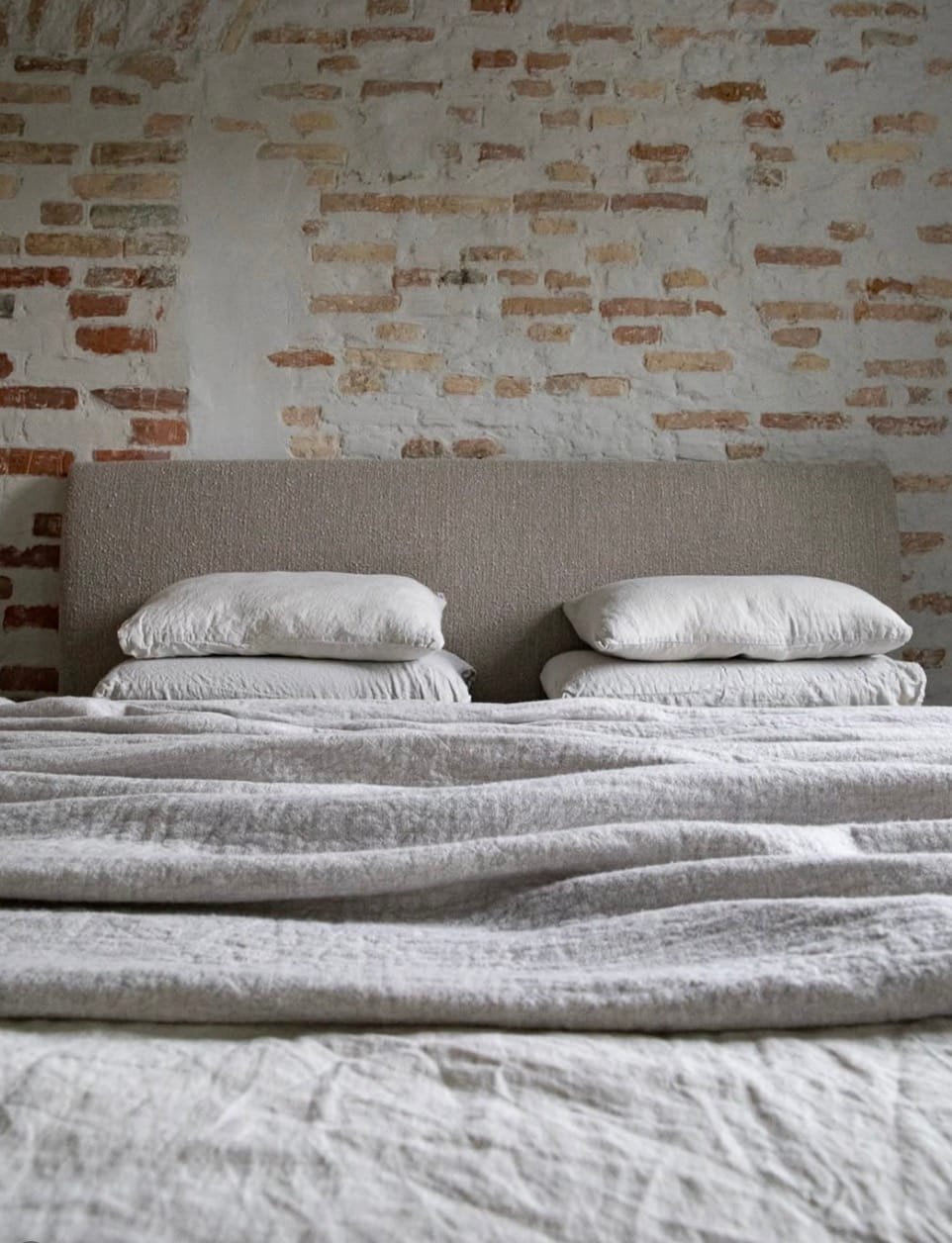 Jauki, sluoksniuota natūralaus lino patalynė miegamajame, žemės spalvų tonai.