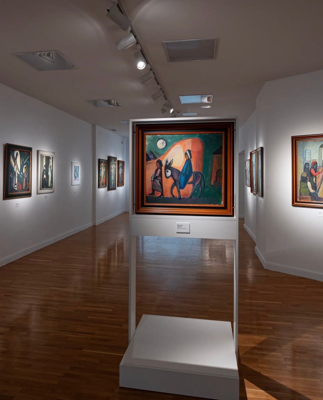 Erdvi meno galerijos salė su ant sienų kabančiais tamsiais ekspresionistiniais paveikslais.