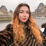 Turinio kūrėja Valerija Kozikaitė šypsosi pozuodama su knyga rankose, spinduliuojanti estetiką ir vidinę ramybę.