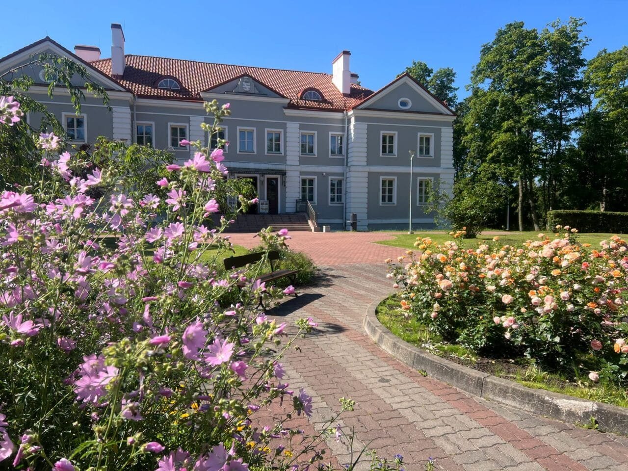 Lietuvos dvarai vasarą: Antazavės dvaro rūmai ir išpuoselėtas angliško stiliaus parkas saulėtą popietę.
