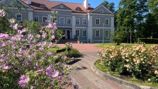 Lietuvos dvarai vasarą: Antazavės dvaro rūmai ir išpuoselėtas angliško stiliaus parkas saulėtą popietę.