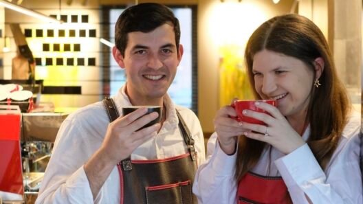 Vyras ir moteris su „Koffee Lab“ prijuostėmis šypsosi ir geria kavą iš puodelių.