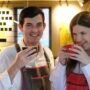 Vyras ir moteris su „Koffee Lab“ prijuostėmis šypsosi ir geria kavą iš puodelių.