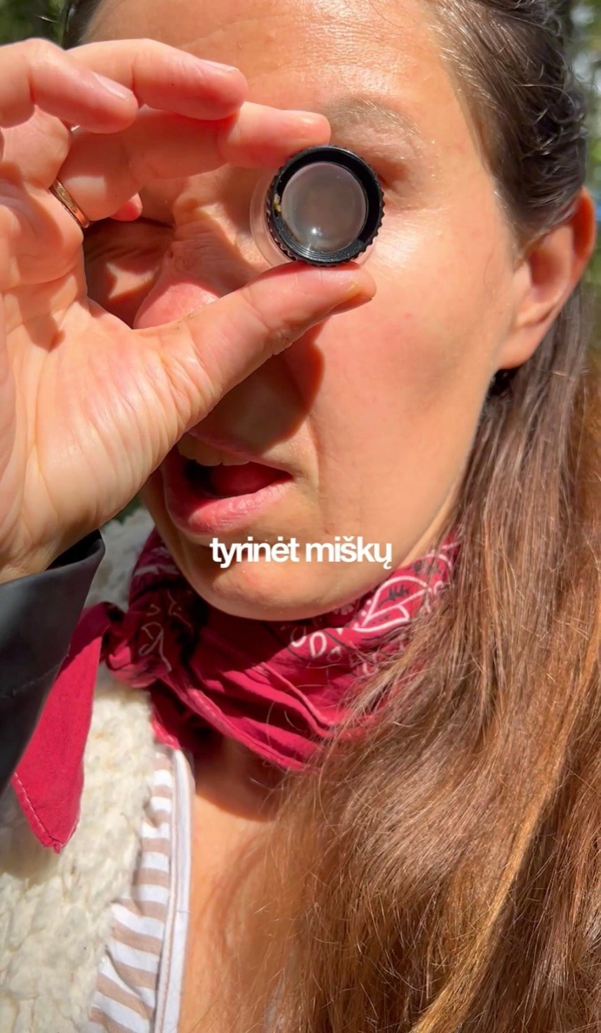Gintarė Petrauskaitė pro lupą žiūri į miško augalus.
