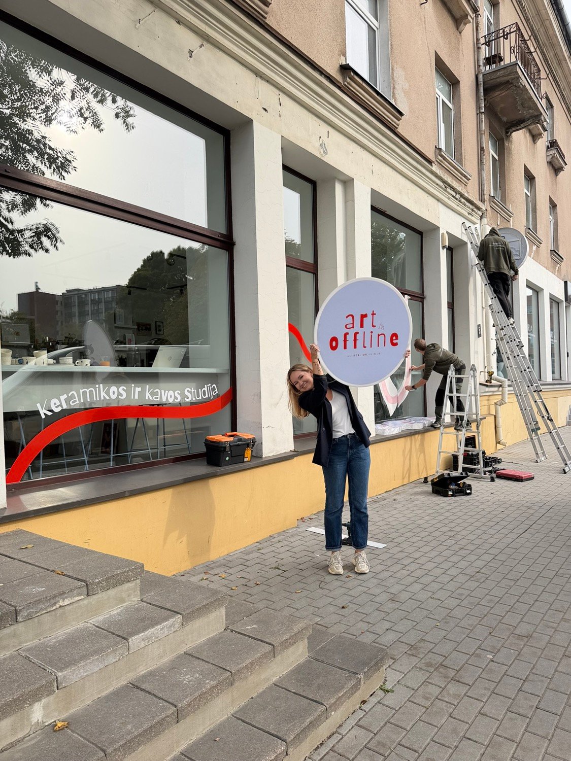 Moteris laiko „Art Offline“ iškabą šalia studijos įėjimo