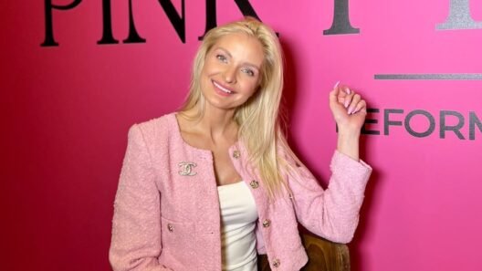 Besišypsanti šviesiaplaukė moteris su rožiniu švarkeliu prie „Pink Pilates“ sienelės