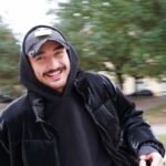 Besišypsantis vaikinas Lukas Karsokas su juoda striuke ir kepure lauke