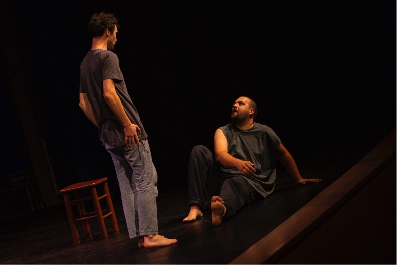 Teatro festivalis pakeleivingi: dviem aktoriams vaidinant tamsioje scenoje spektaklio akimirka