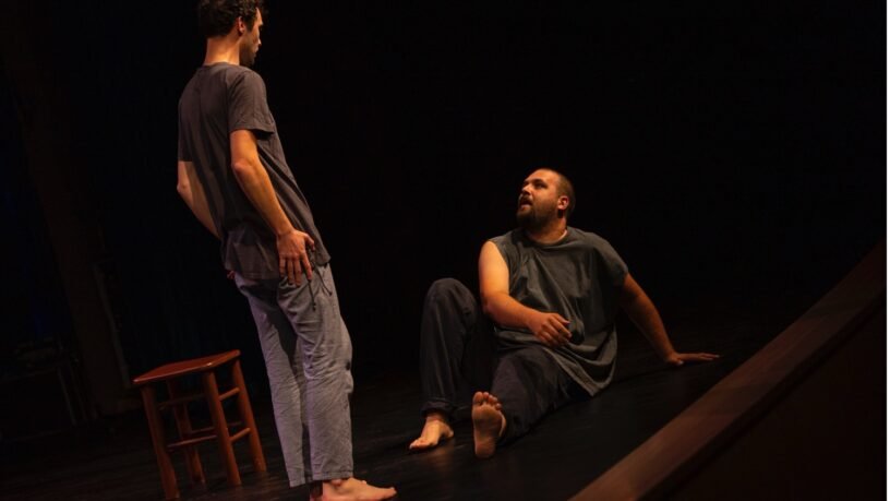 Teatro festivalis pakeleivingi: dviem aktoriams vaidinant tamsioje scenoje spektaklio akimirka