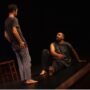 Teatro festivalis pakeleivingi: dviem aktoriams vaidinant tamsioje scenoje spektaklio akimirka